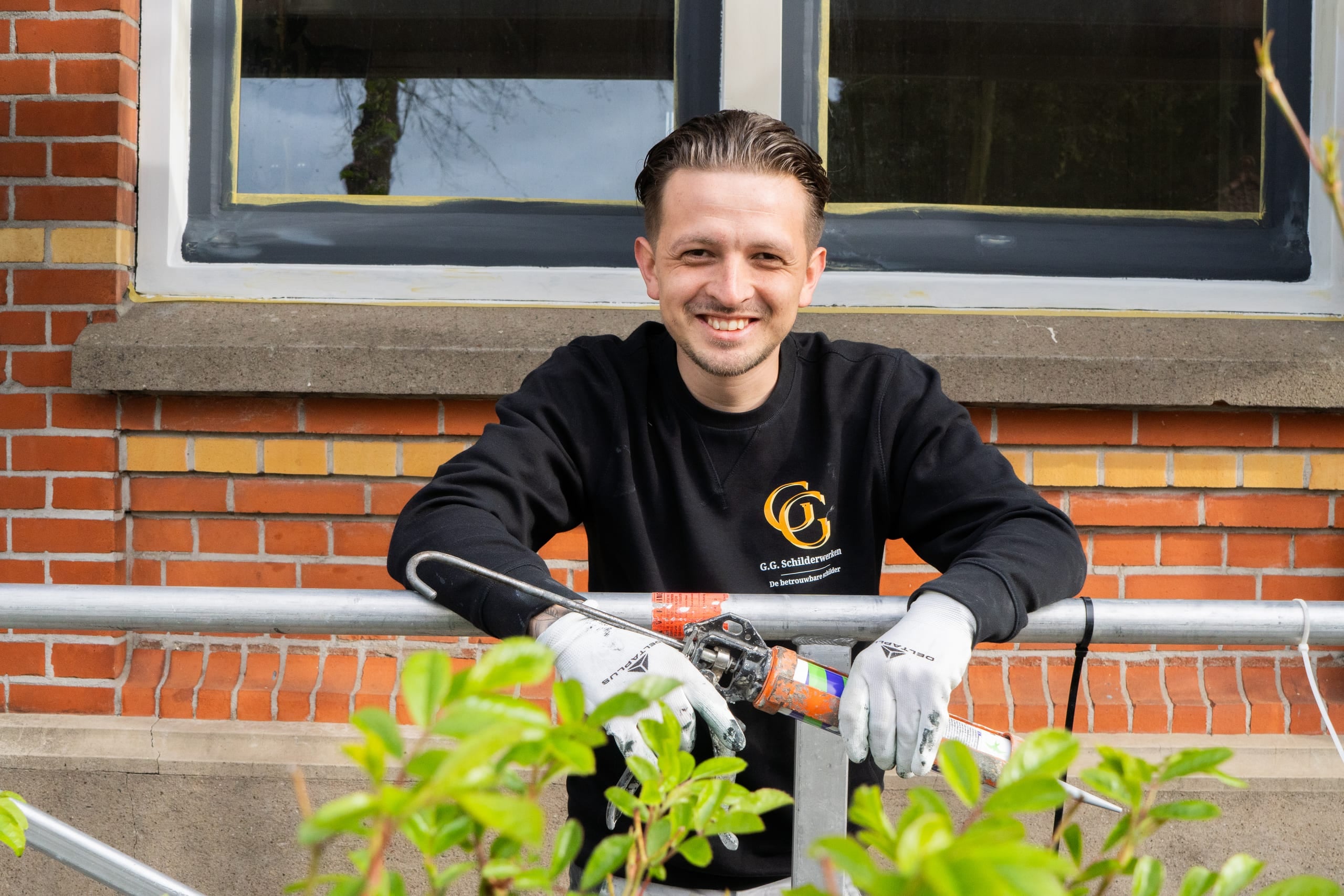 Lachende schilder van G.G. Schilderwerken achter zijn gereedschap bij een raamkozijn