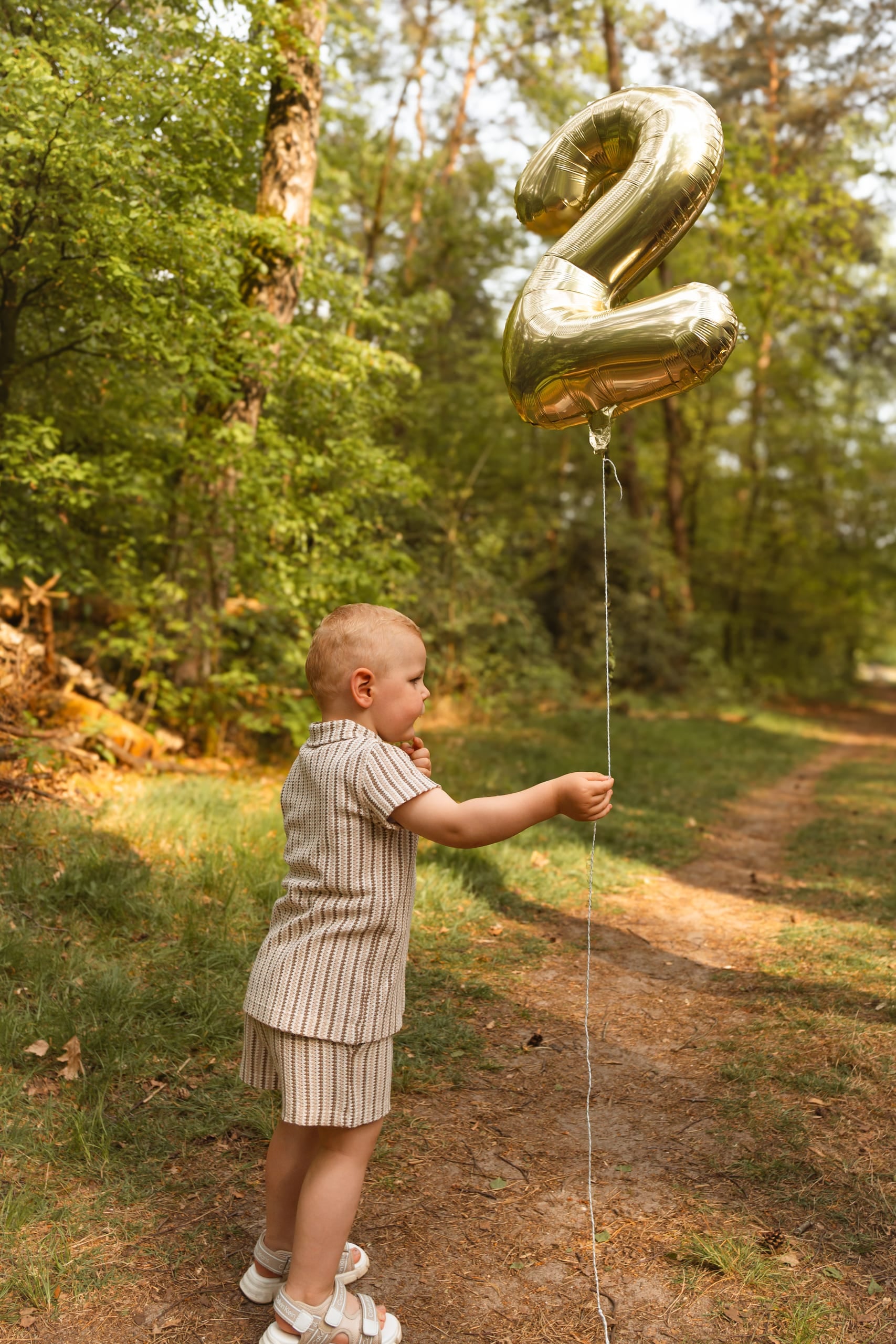 Jongetje houdt een gouden ballon in de vorm van een twee vast op een bospad