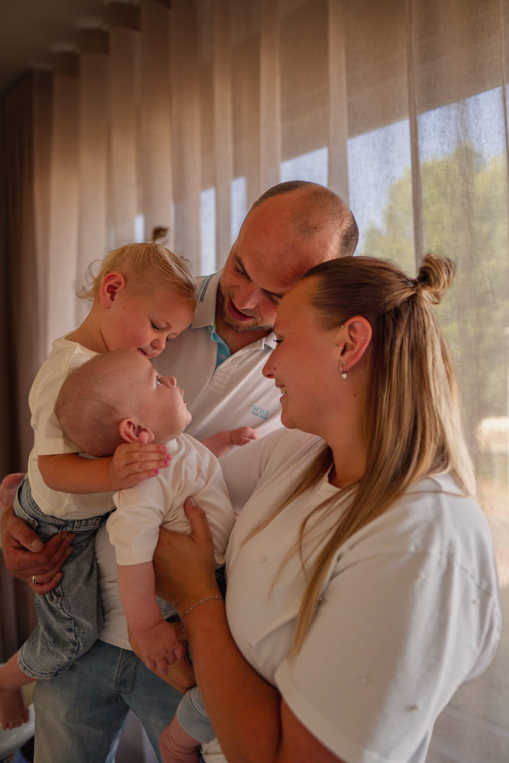 Ouders met hun peuter en baby in tegenlicht voor het raam