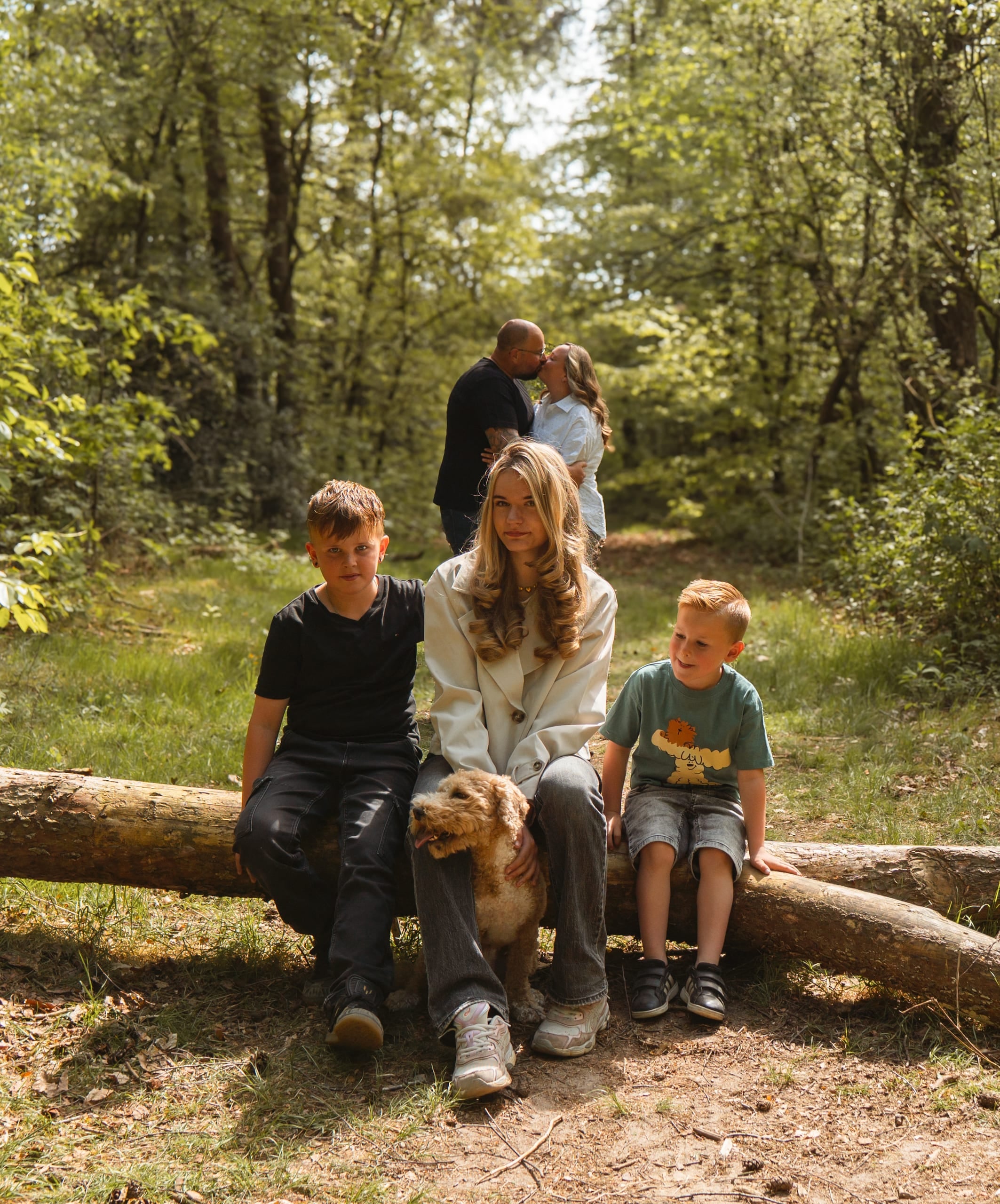Moeder met haar twee zoons en de hond op een omgevallen boomstam in het bos