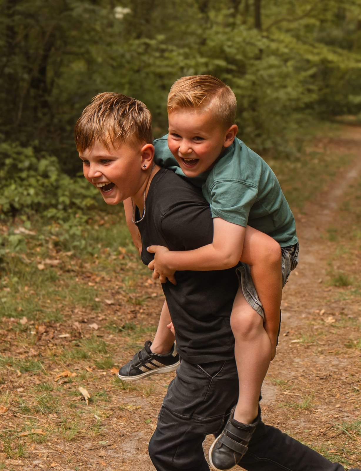 Twee broers rennen lachend over een bospad, de jongste op de rug