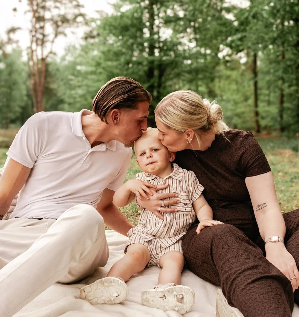 Ouders geven hun zoontje een kus tijdens een gezinsshoot in het bos