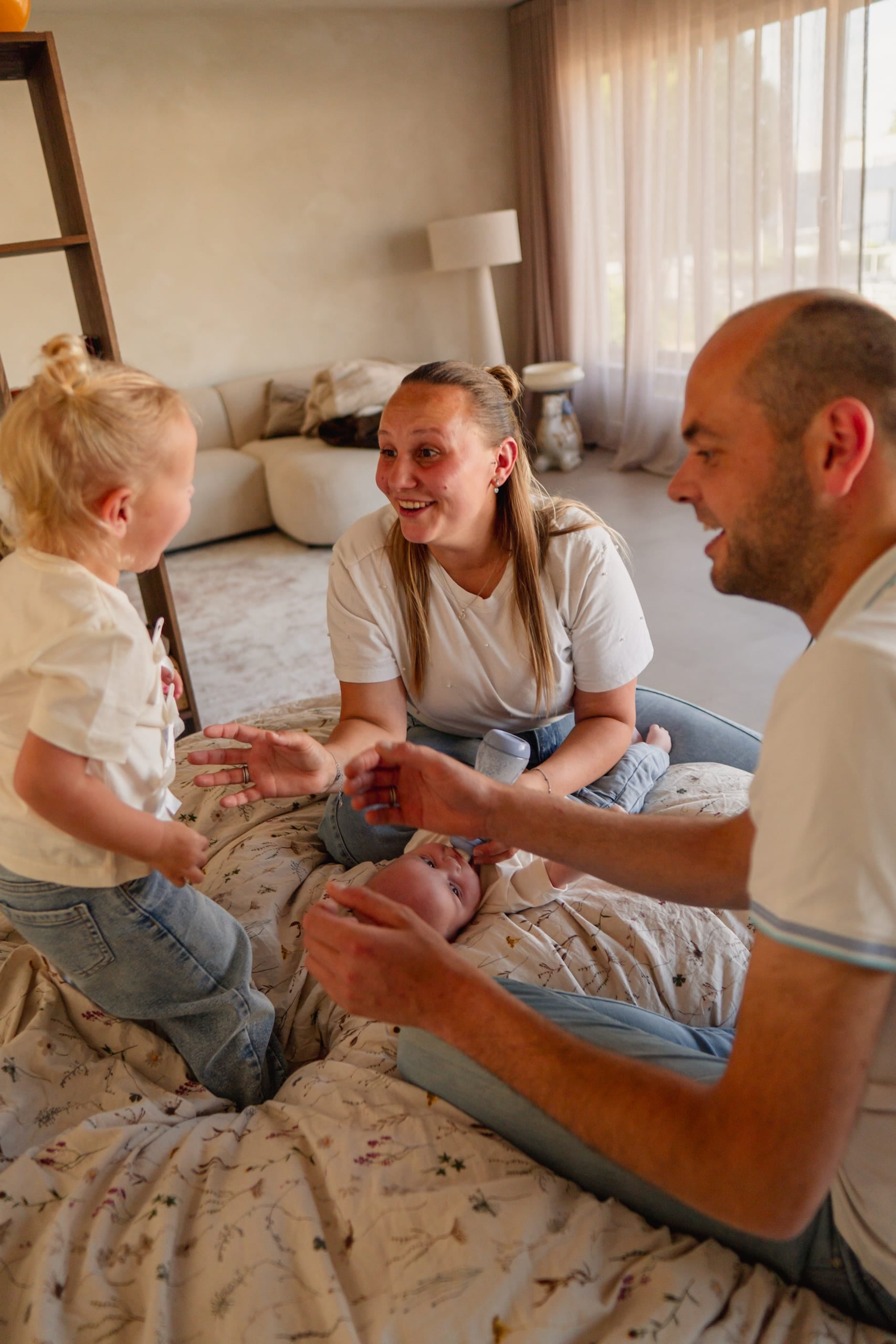 Ouders spelen met hun peuter en baby op bed, thuis in de slaapkamer
