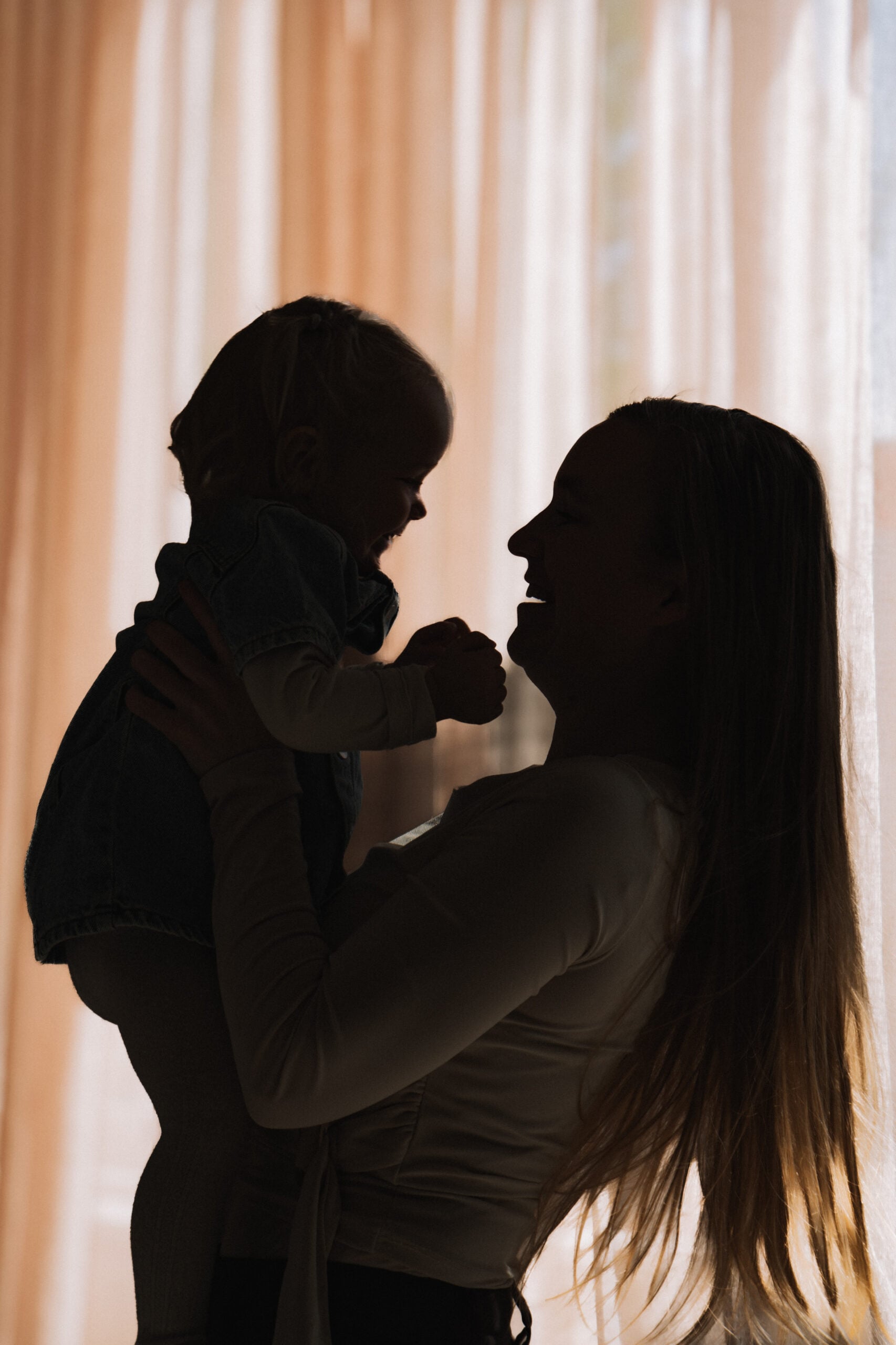 Silhouet van een moeder die haar baby omhoog houdt voor een raam