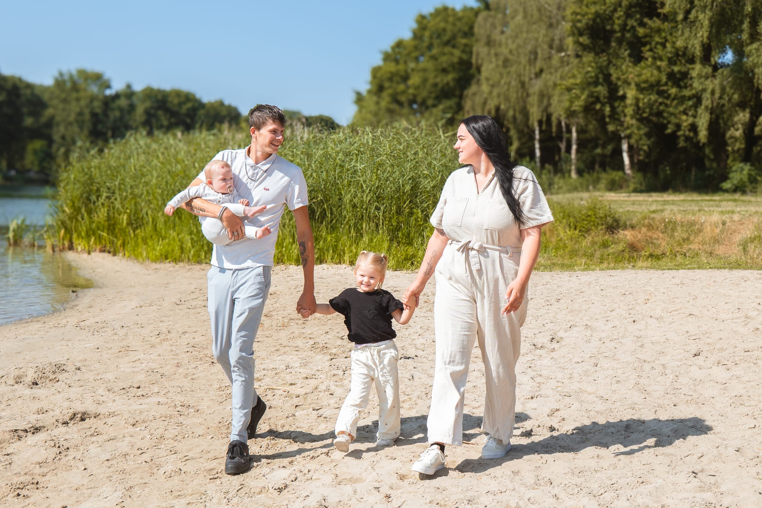 Gezin wandelt over het strand langs het water, vader met baby op de arm