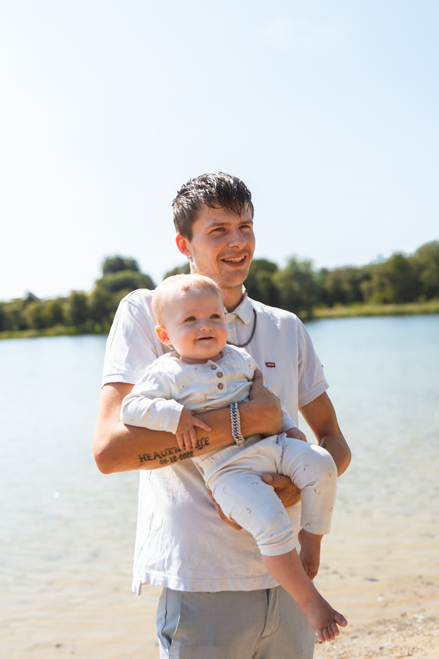 Vader houdt zijn baby vast aan de waterkant op een zonnige dag