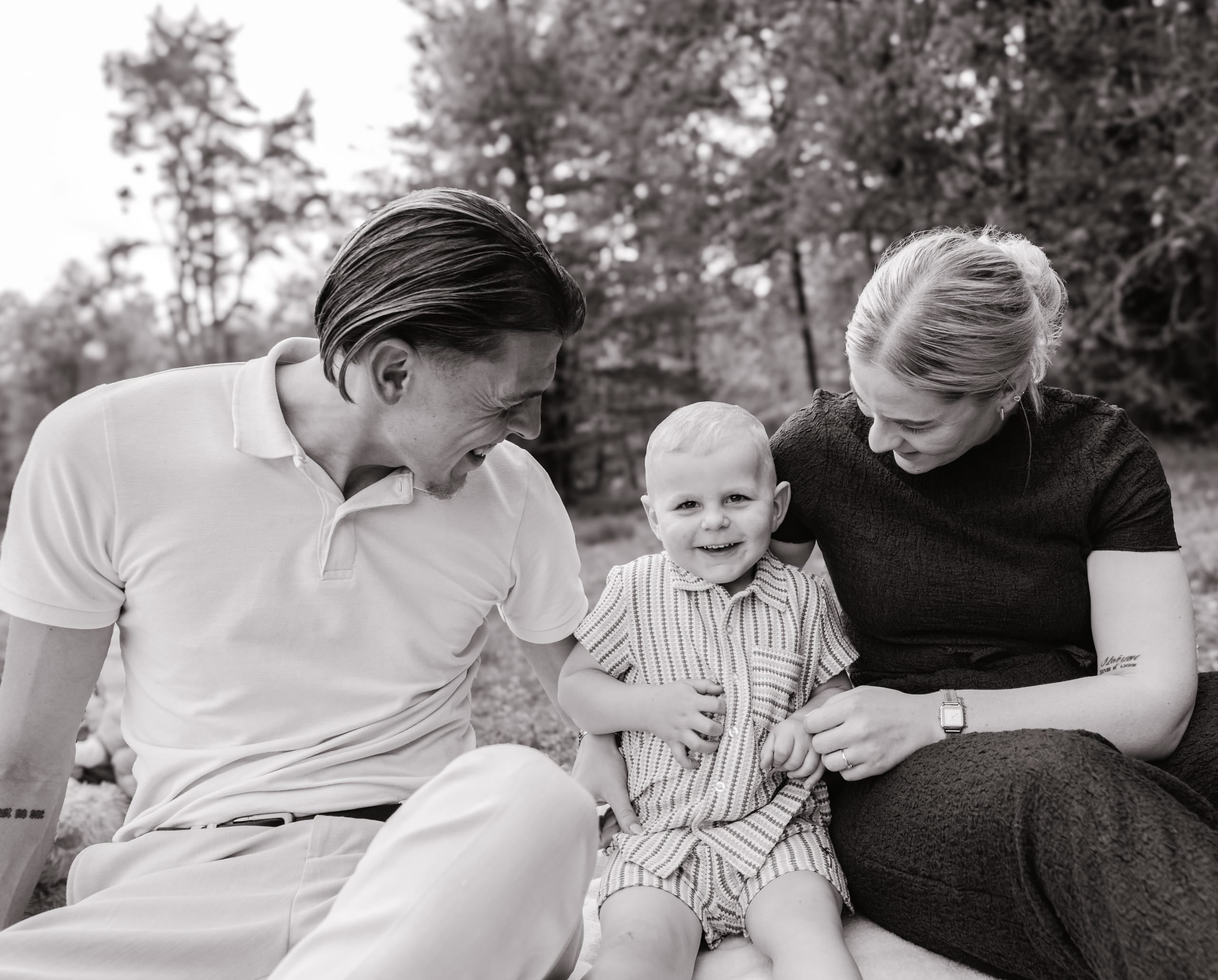 Zwart-witfoto van ouders die lachen naar hun peuter tussen hen in