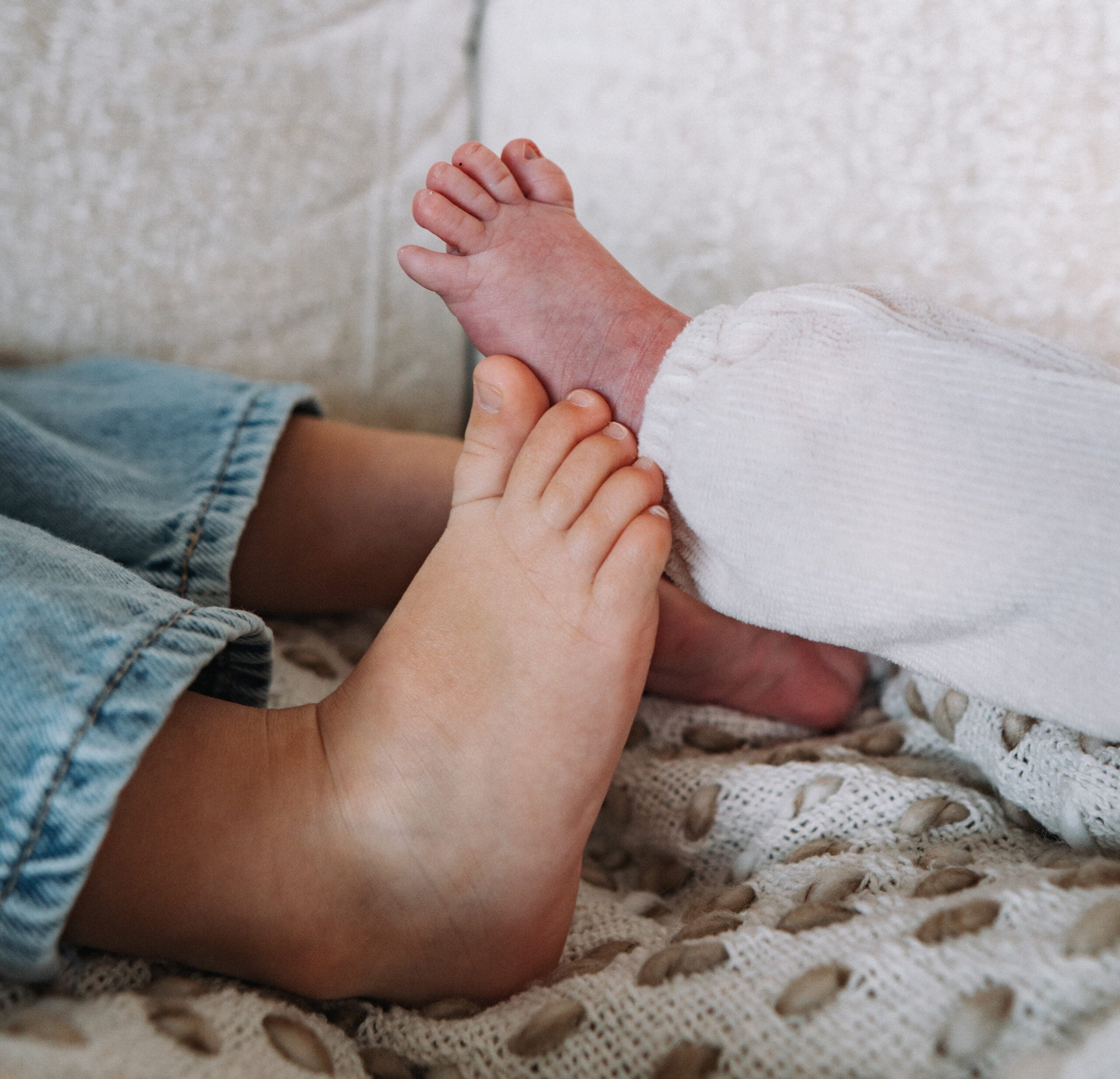 Voetjes van een pasgeboren baby naast die van een groter kind op een deken