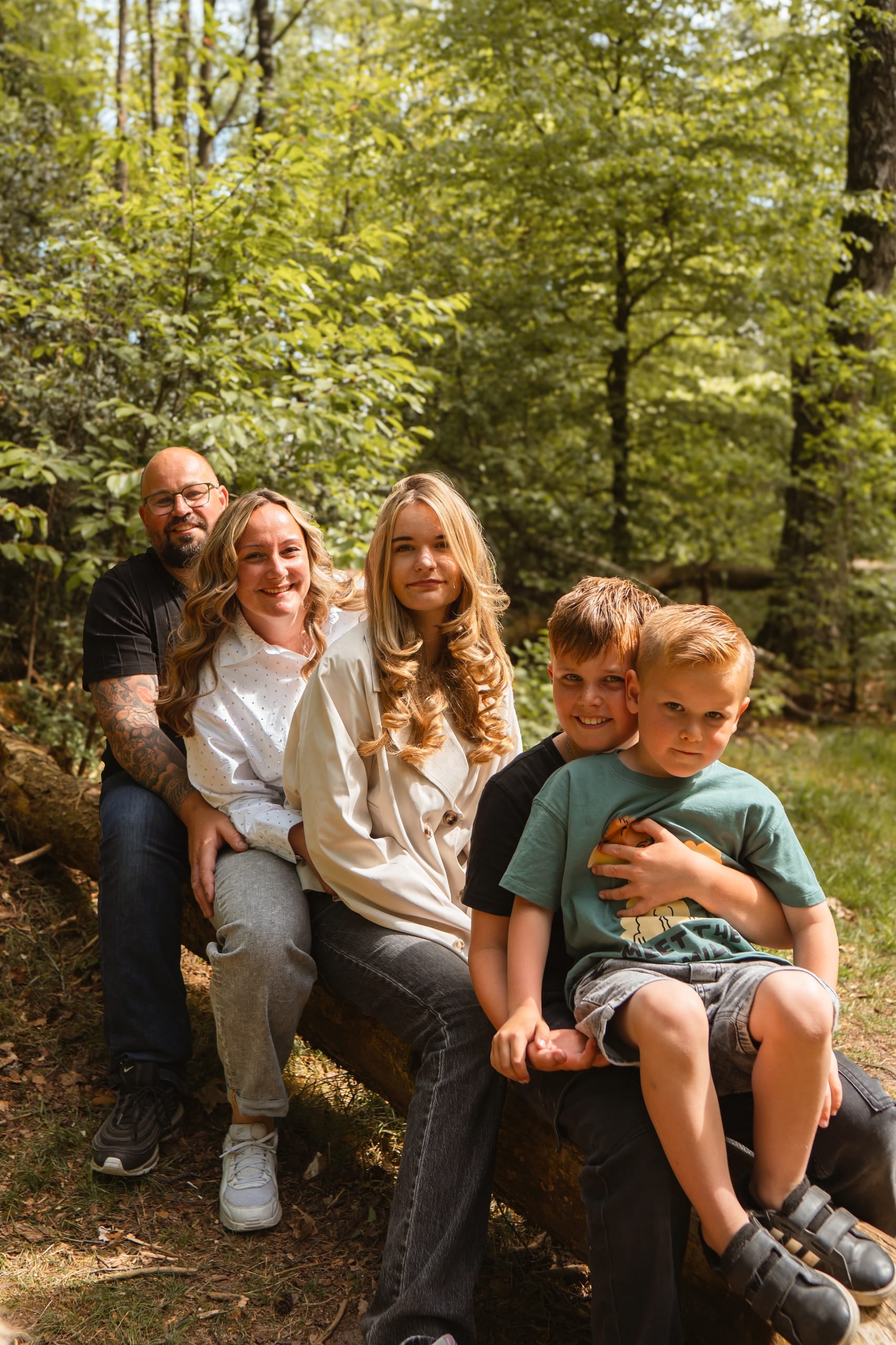 Gezin van vijf zit samen op een boomstam in het bos tijdens een gezinsshoot bij Deventer